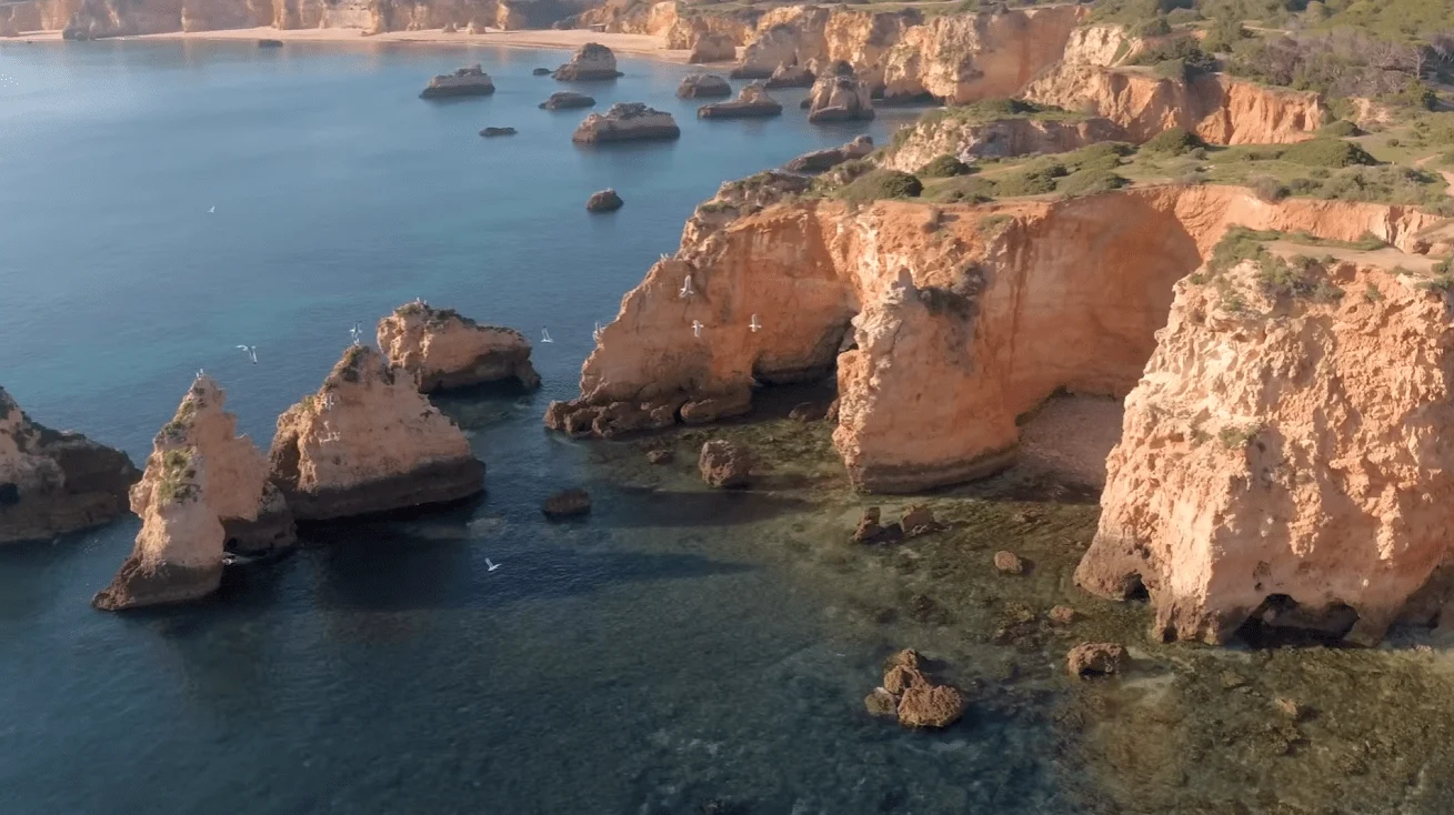 Orange sandstone cliffs and sea stacks along a rocky coast