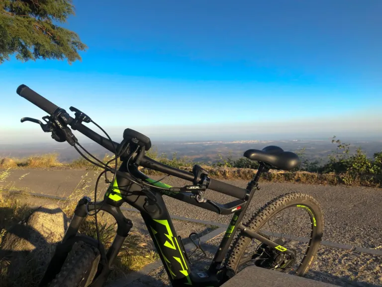 Black e-bike with green accents parked at a hilltop viewpoint with a hazy valley below