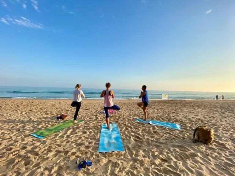 Three people doing yoga poses on a beach