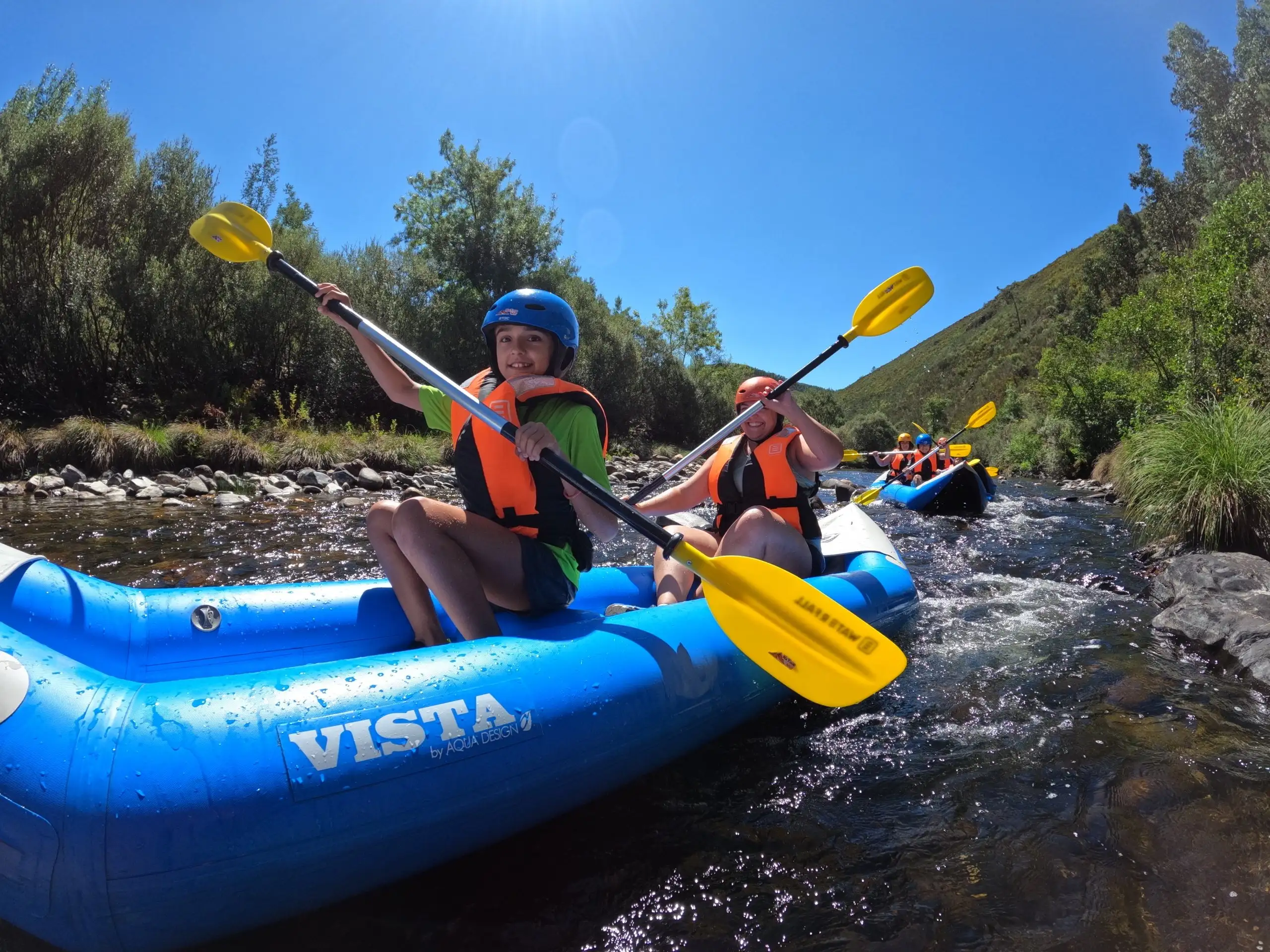 Two kayakers in helmets paddling a blue inflatable kayak through rapids