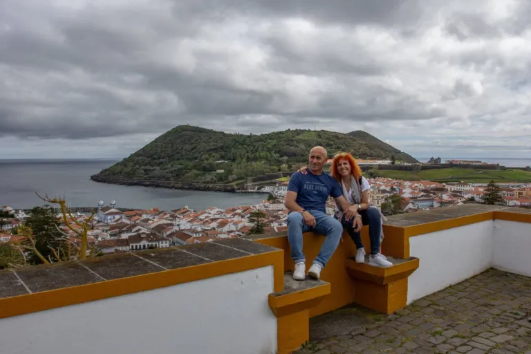 Couple sitting on a white wall with a view of a hilltop and town on the coast