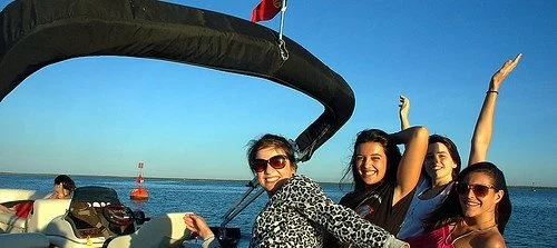 Group of women cheering on the bow of a boat with a canopy overhead