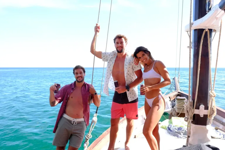 Three friends smiling on the deck of a wooden sailing boat