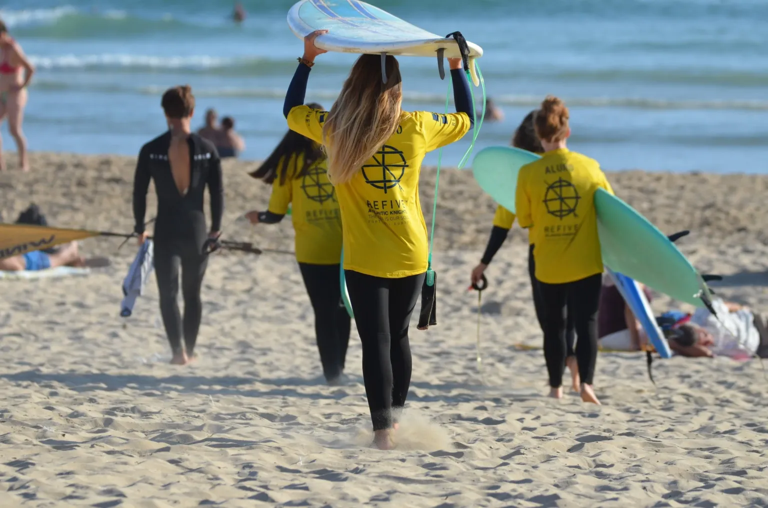Surf instructors in yellow tops carrying boards along the beach