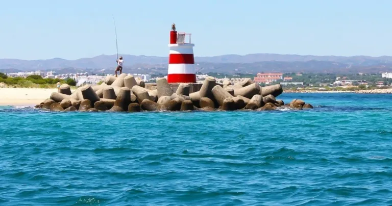Red-and-white striped lighthouse on a rocky breakwater with a town behind