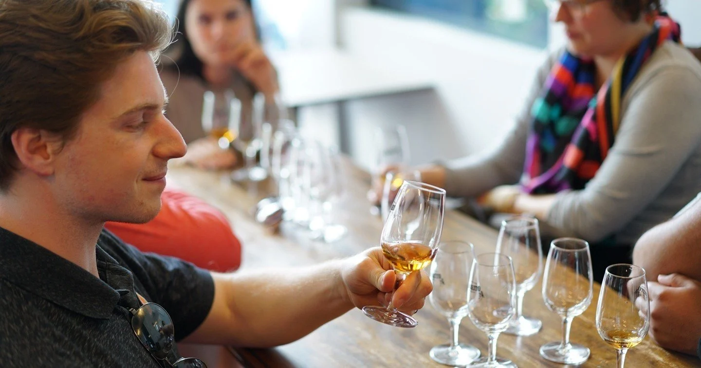 Man holding a glass at a long table set with rows of tasting glasses