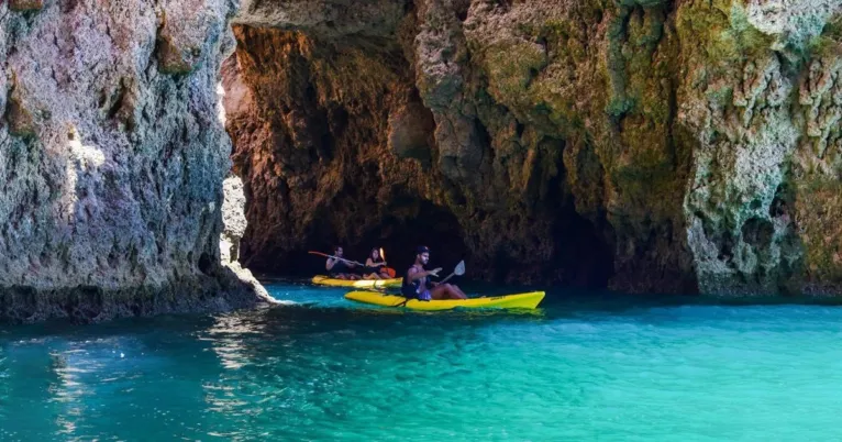 Kayakers paddling out from a cave opening in a cliff