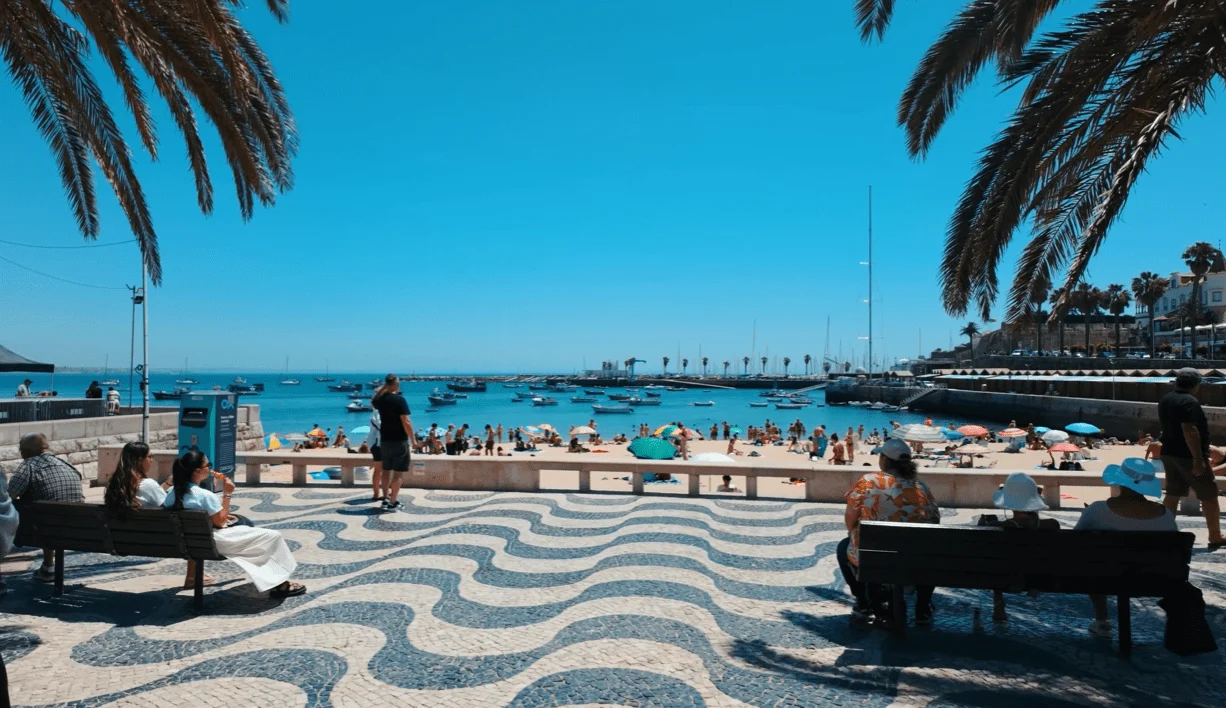 Wave-patterned promenade with benches and palm trees facing a harbour beach