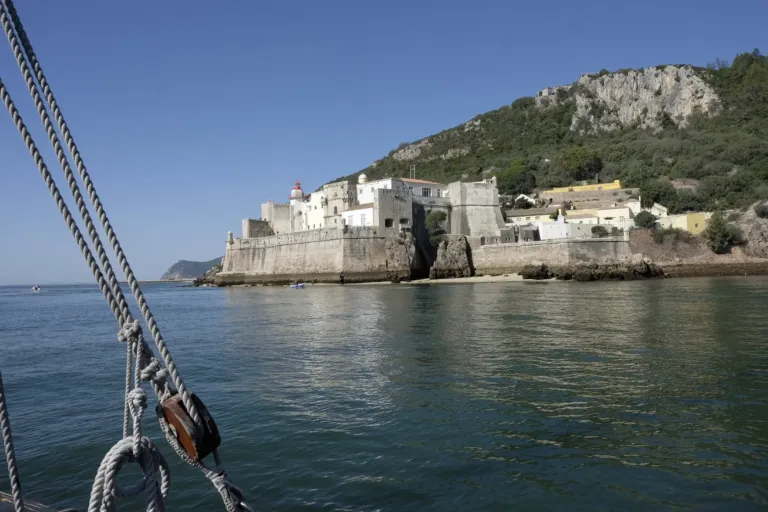 Whitewashed fortified buildings on a headland seen from a sailing boat