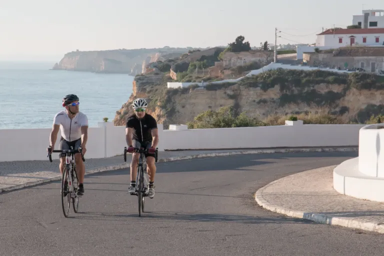 Two road cyclists riding along a cliff-top road above the sea