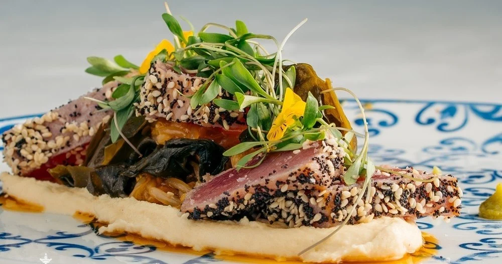 Plated tuna with sesame crust, microgreens and puree on a blue-patterned plate