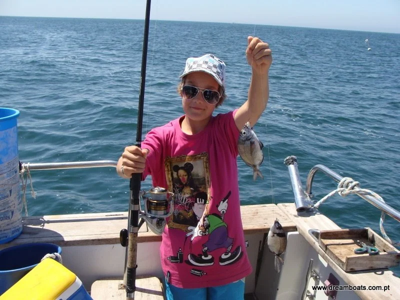 Child in a sun hat holding up a small fish on a boat