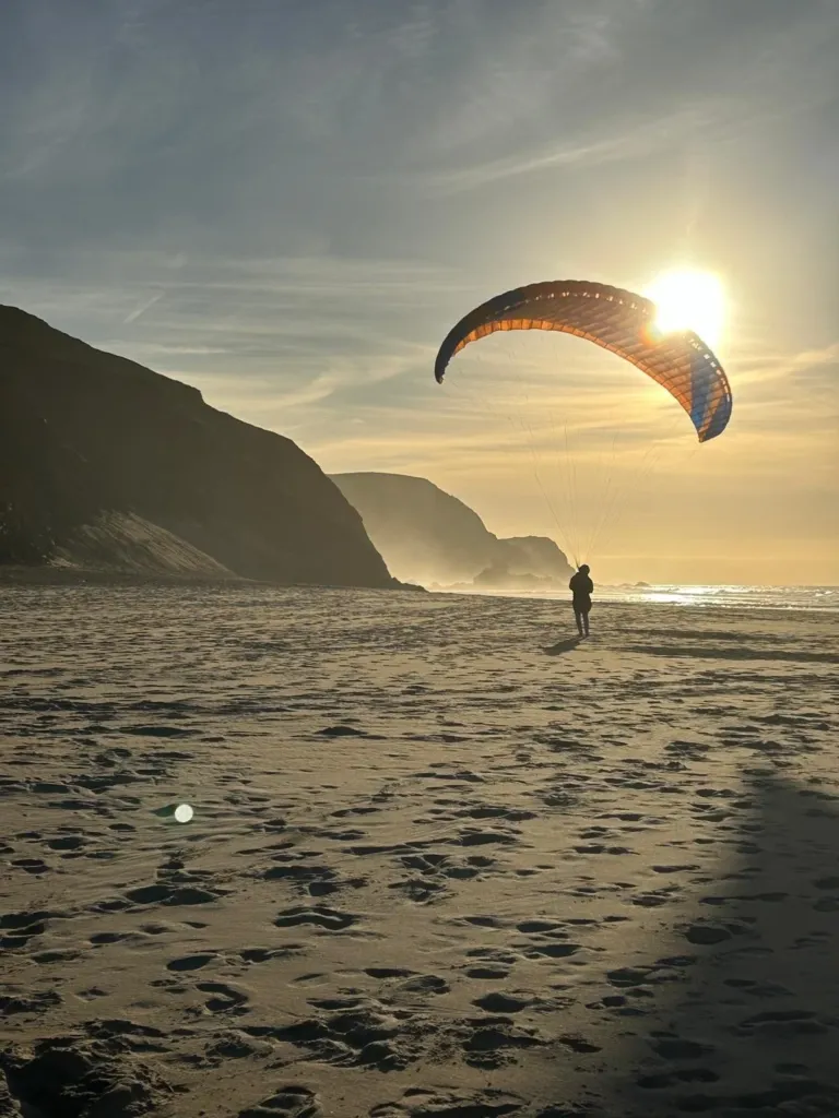 Paraglider silhouetted against the sun above a beach