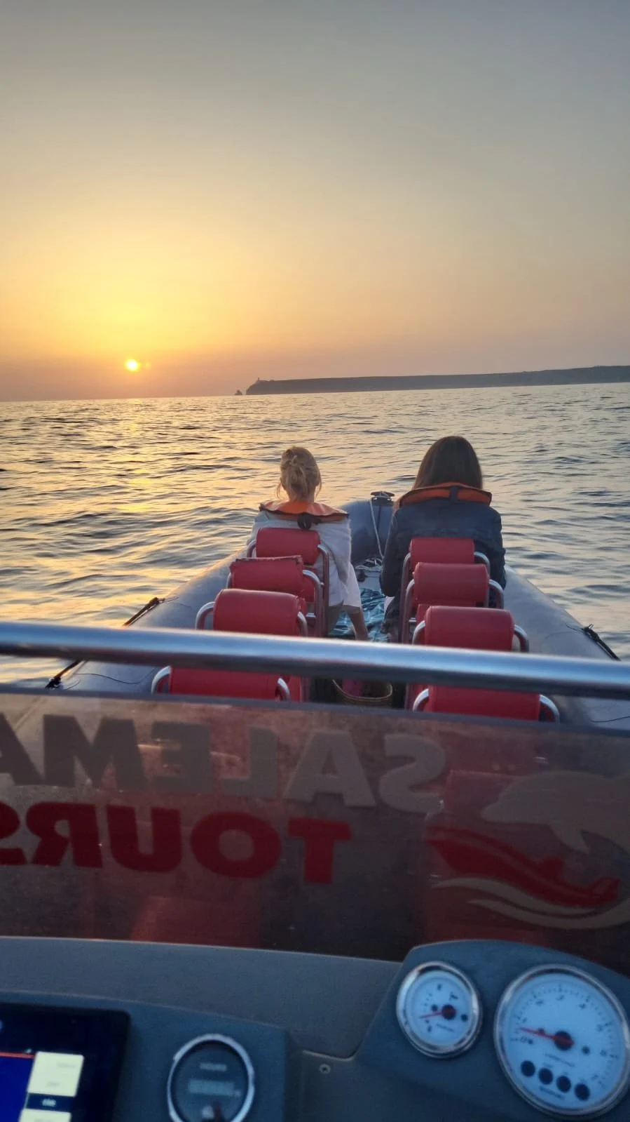 Two passengers on red seats of a speedboat watching the sun set over the sea
