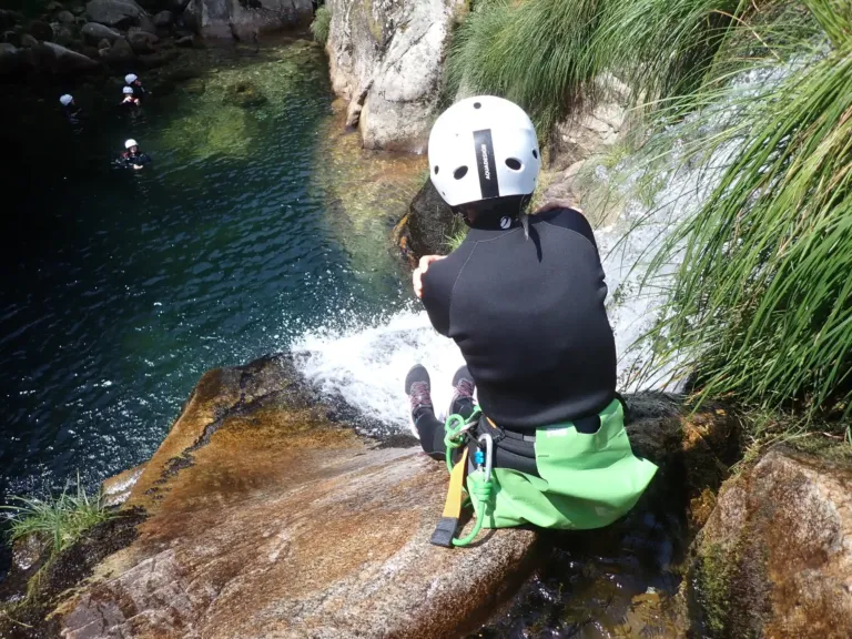 Canyoner in a helmet seated on a rock at the top of a waterfall pool