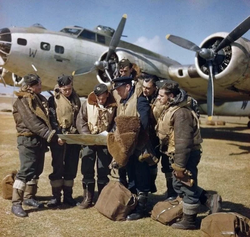 Crew in flight gear studying a map beside a vintage bomber aircraft