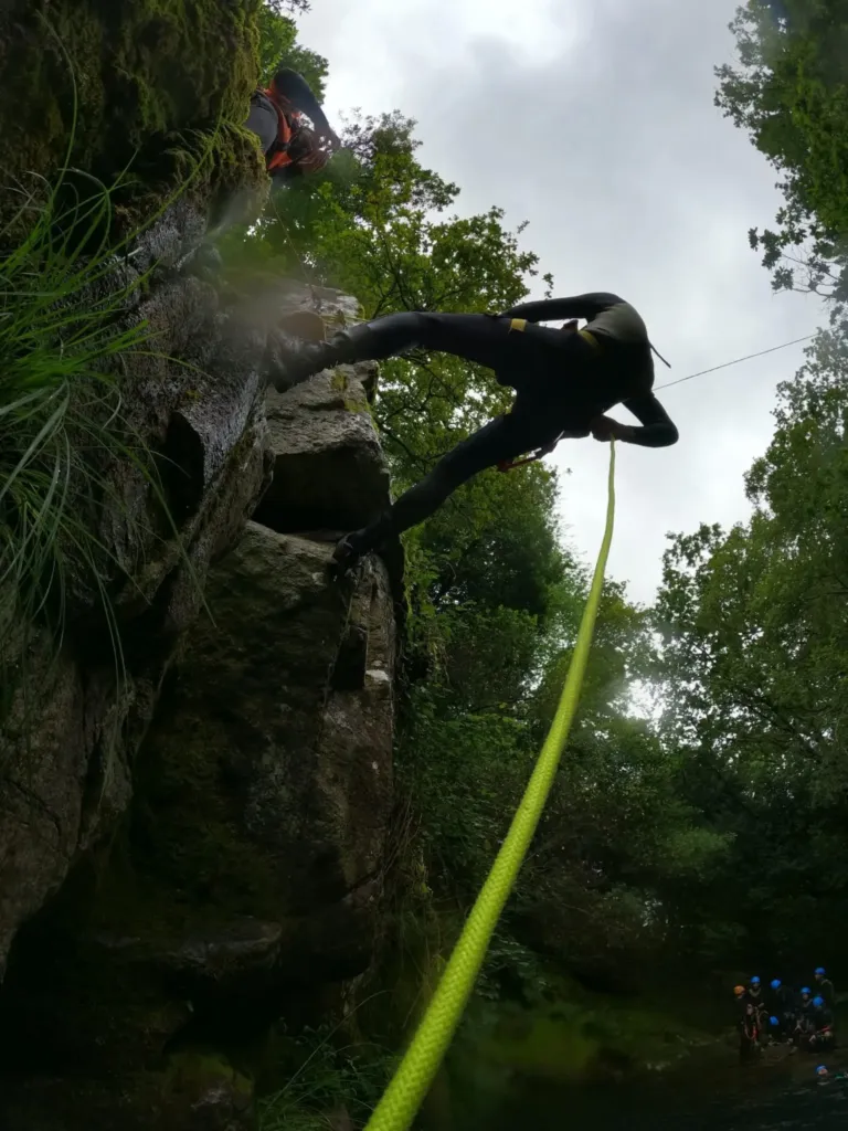 Canyoner swinging from a rope in a green gorge