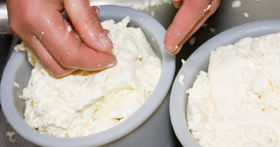 Hands working fresh cheese in two bowls