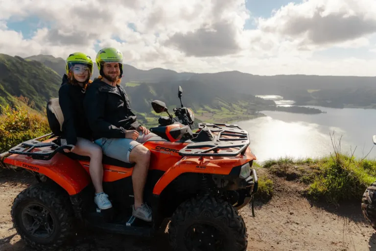 Couple in helmets on an orange quad bike beside a crater lake