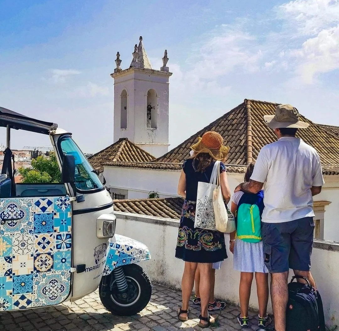 Family beside a tile-decorated tuk-tuk with a church tower behind